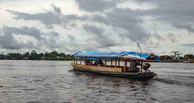 Bateau avec un auvent sur une rivière, ciel nuageux en arrière-plan.