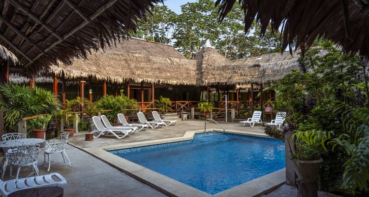 Zone de villégiature avec une piscine entourée de flore tropicale et de structures en bois.