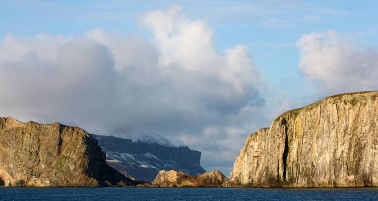 Rotsachtige kliffen met bewolkte lucht boven de oceaan.
