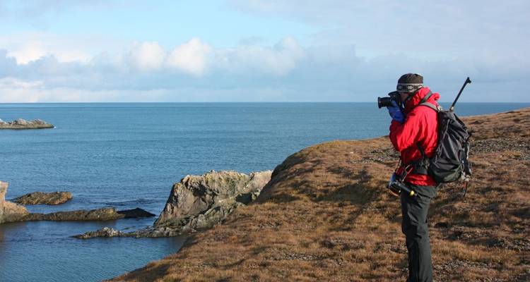 Persoon in rode jas die foto's maakt bij de klifkust.