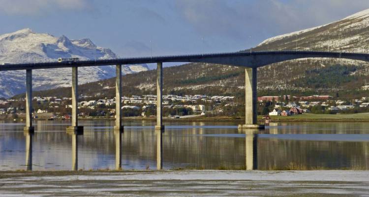 Brug over een rivier met besneeuwde bergen op de achtergrond.