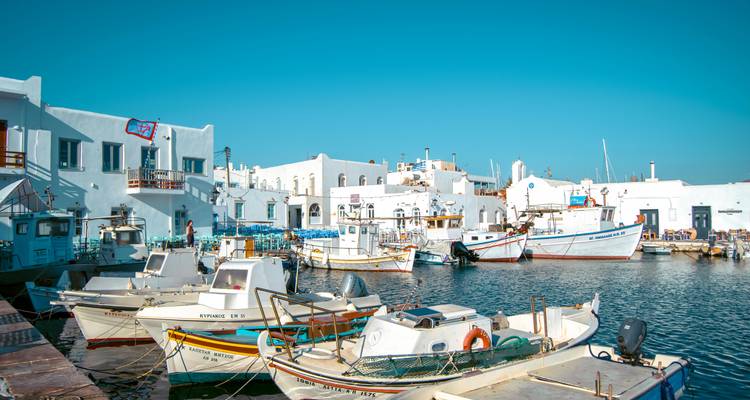 Bateaux amarrés dans un port grec animé avec des bâtiments blancs.