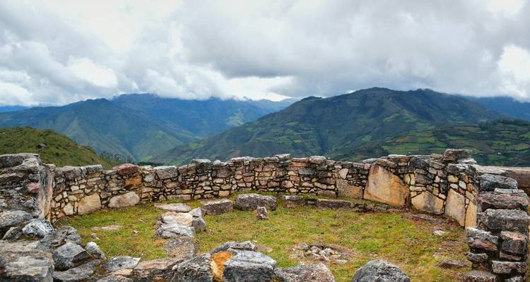 Estructura de piedra circular en una colina con un telón de fondo montañoso.