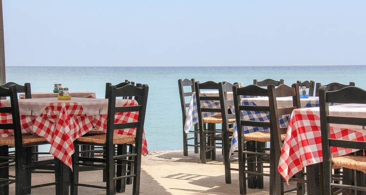 Tables extérieures en bord de mer avec nappes à carreaux donnant sur l'océan.
