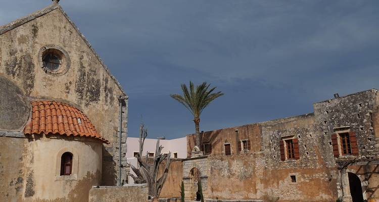 Anciens bâtiments en pierre avec un palmier sous un ciel nuageux.