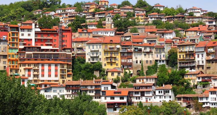 Colorful hillside houses stacked on steep terrain amid greenery in Veliko Tarnovo.