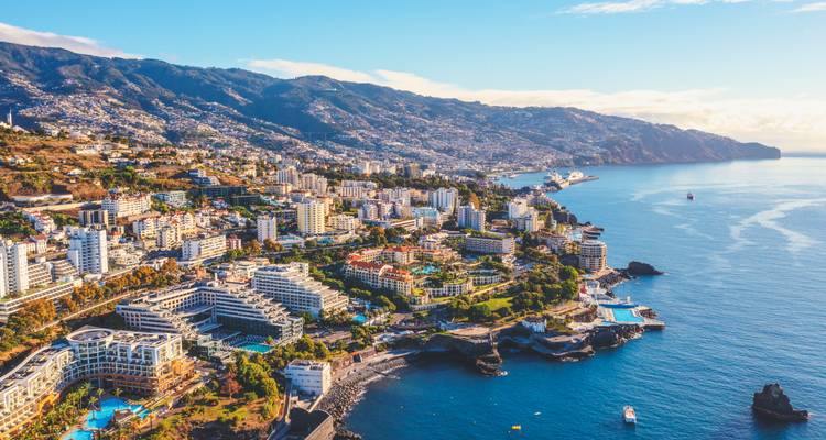 Vista aérea bañada por el sol de los resorts en los acantilados de Funchal, costa escarpada y el telón de fondo del Océano Atlántico en Madeira.