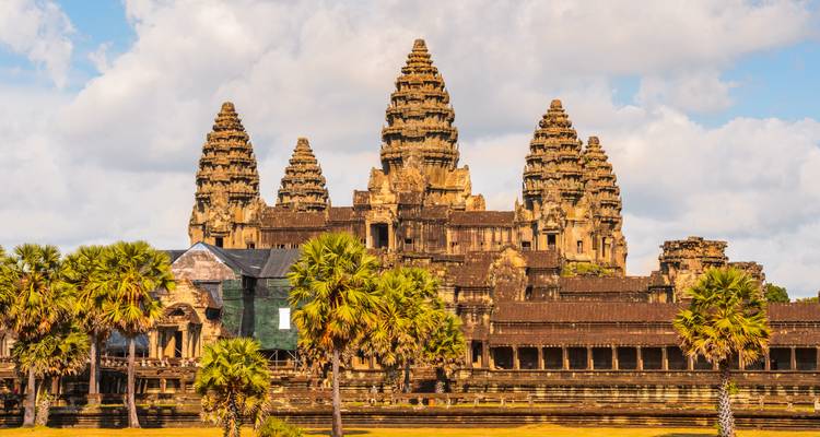 Vue de face du complexe emblématique du temple d'Angkor Vat encadré par des palmiers sous un ciel bleu