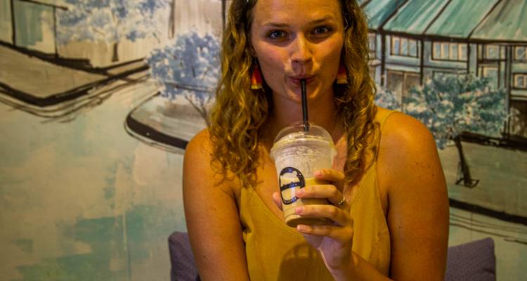 Jeune femme sirotant une boisson froide avec une paille dans un café chaleureux avec une fresque murale en arrière-plan