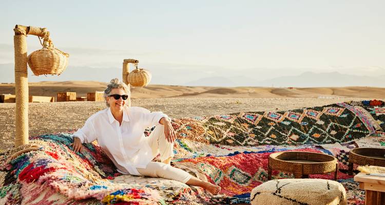 Mujer sentada sobre alfombras coloridas en un entorno desértico.