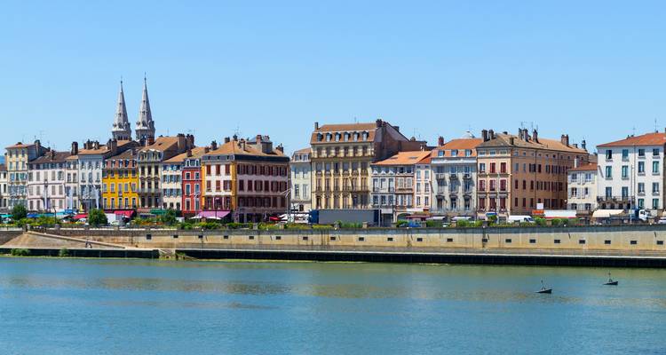 Kleurrijke rij historische gebouwen aan de rivier weerspiegeld in kalm water onder een heldere blauwe hemel.