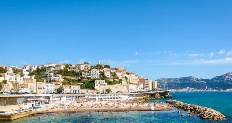 Een zandstrand met bezoekers en huizen op de heuvelrand in Marseille.