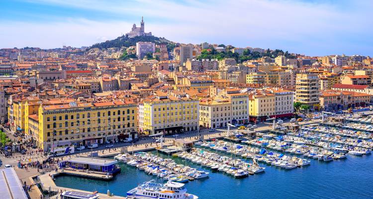 Vue aérienne vibrante du Vieux-Port de Marseille rempli de yachts, bâtiments pastel et Notre-Dame de la Garde au sommet de la colline.