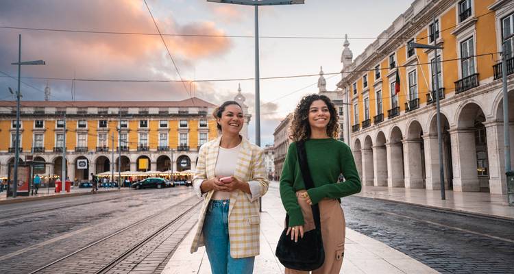 Deux femmes marchant sur une place historique avec des rails de tramway à Lisbonne.