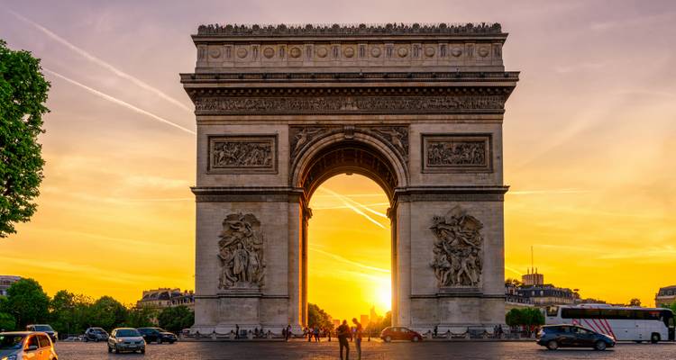 Arc de Triomphe silhouetted against a brilliant golden sunset with light streaming through the arch.