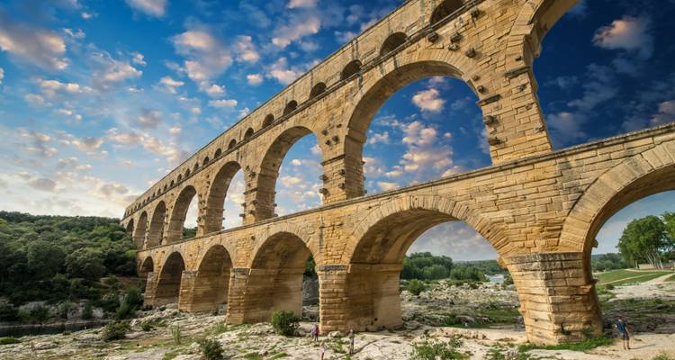 Ancient aqueduct spanning across a river landscape with a blue sky backdrop.