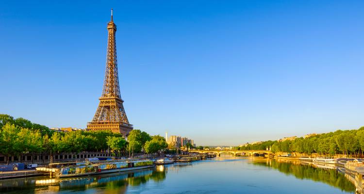 Vista icónica de la Torre Eiffel reflejándose en el río Sena bajo un cielo matutino azul despejado.