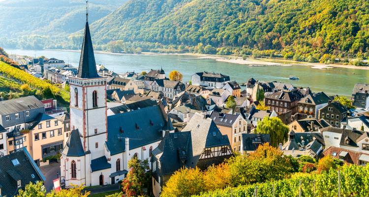 Charming Rhine gorge village with church spire, vineyards and river framed by forested hills.