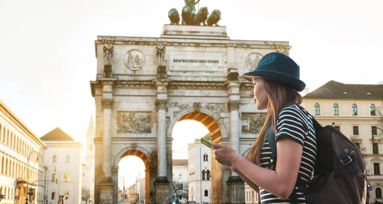 Jeune voyageur avec sac à dos étudie son téléphone devant l'arc de triomphe de Munich, le Siegestor.