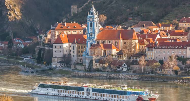 Un bateau de croisière fluviale navigue devant l'abbaye pittoresque aux tours bleues et les toits de terre cuite de Dürnstein sur le Danube.