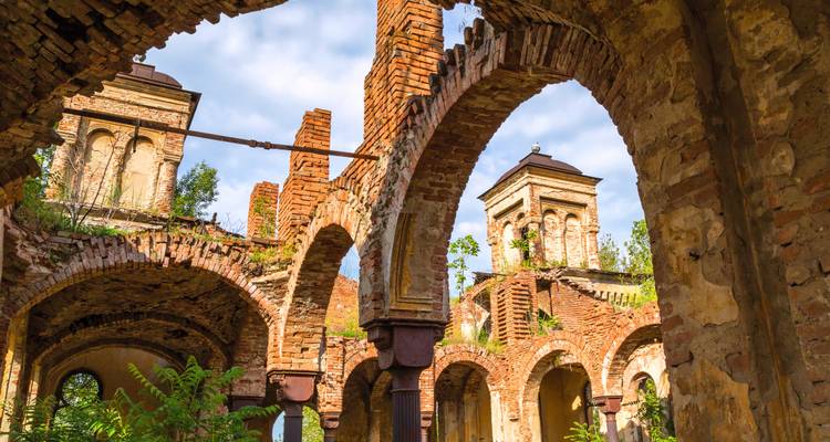Crumbling brick arches and towers of an abandoned historic building against a blue sky