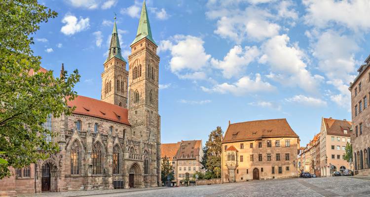 Quiet square with twin-towered medieval church and surrounding historic buildings under a blue sky in Nuremberg.