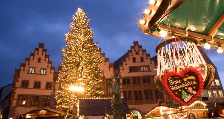 Scène de marché de Noël du soir avec sapin scintillant et décoration de cœur en pain d'épice devant des bâtiments à colombages.