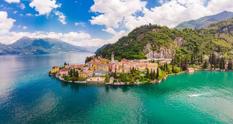 Panorama aérien d'un village coloré au bord d'un lac sur une péninsule entourée d'eaux turquoise et de montagnes luxuriantes