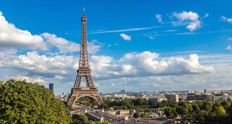 Vue de jour de la tour Eiffel qui domine Paris avec des nuages cotonneux et le paysage urbain.