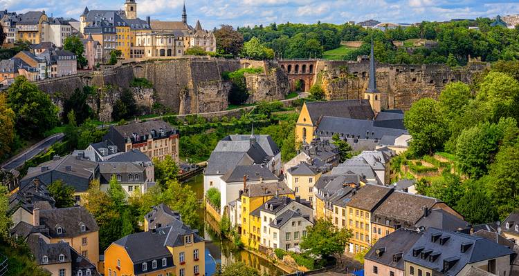 Vue panoramique sur les fortifications historiques de Luxembourg-Ville et les maisons pastel nichées dans une vallée luxuriante.