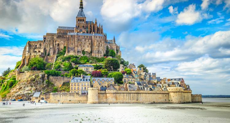 Majesteitelijke abdij Mont Saint-Michel die boven getijdevlaktes en middeleeuwse stenen muren uittorent onder heldere wolken.