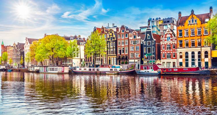 Rangée de maisons traditionnelles d'Amsterdam et de péniches se reflétant dans un canal sous un soleil éclatant