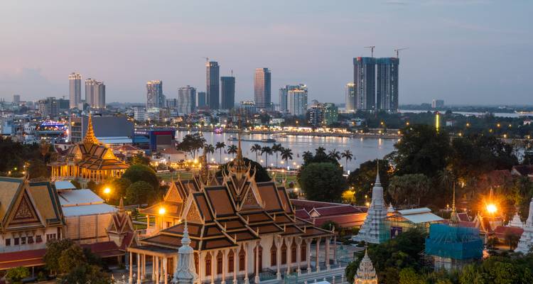 Horizonte del atardecer de Phnom Penh con templos en primer plano y torres modernas más allá del río.