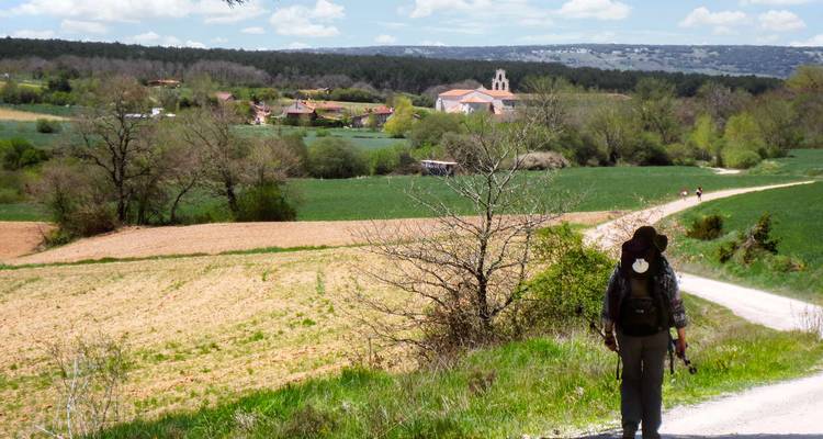 Excursionista con mochila caminando por un sendero hacia un pueblo.