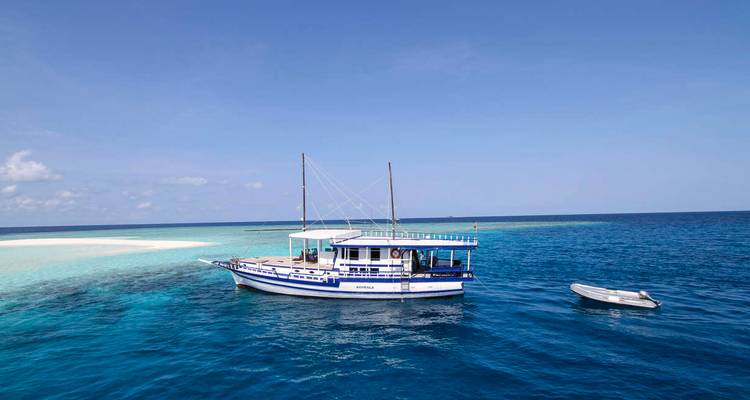 Bateau traditionnel en bois ancré dans un lagon turquoise cristallin à côté d'un petit îlot de sable