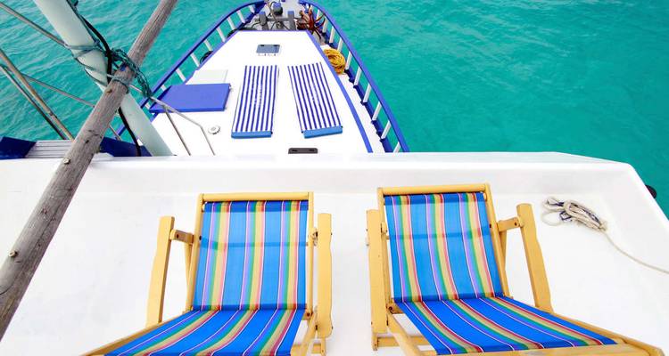Deux chaises longues rayées sur le toit du bateau surplombant un lagon turquoise éclatant