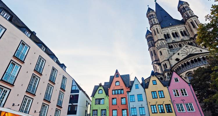 Row of pastel medieval gabled houses beside towering Great St. Martin Church in Cologne.
