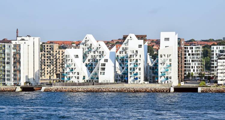 Auffällige moderne weiße Wohnblöcke, bekannt als Der Eisberg, stehen entlang einer Uferpromenade unter klarem Himmel.