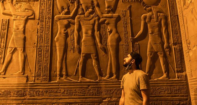 Une personne observant des sculptures murales de l'Égypte ancienne éclairées par des lumières chaudes.