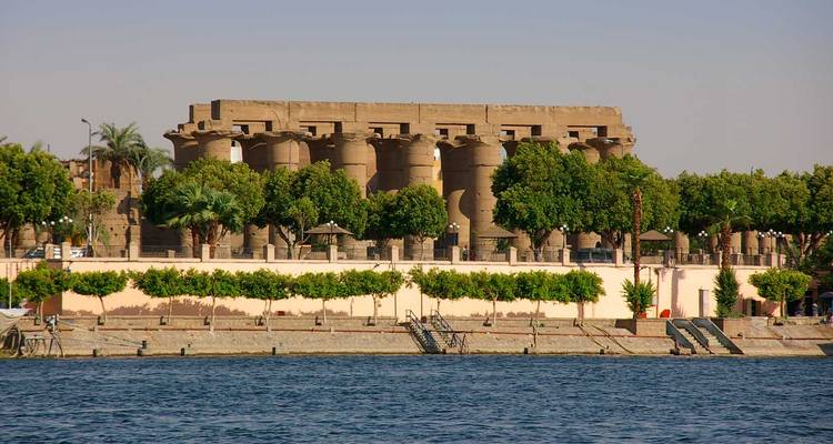 Luxor Temple’s massive columns rising behind a riverside promenade lined with lush trees.