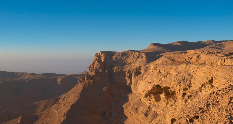 Rugged golden cliffs and desert plateau overlooking vast arid landscapes under a clear blue sky.