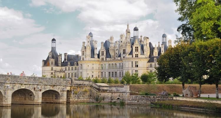 Het majestueuze Château de Chambord rijst op boven een stenen brug en rustige slotgracht onder een gedeeltelijk bewolkte hemel