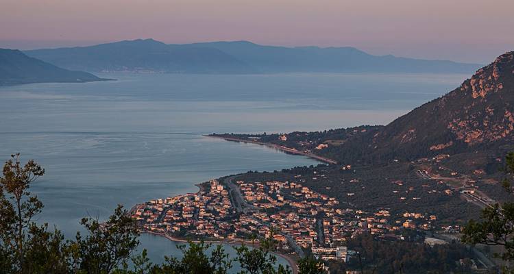Vue douce du crépuscule sur une ville côtière grecque et un long littoral sinueux avec des montagnes en arrière-plan.