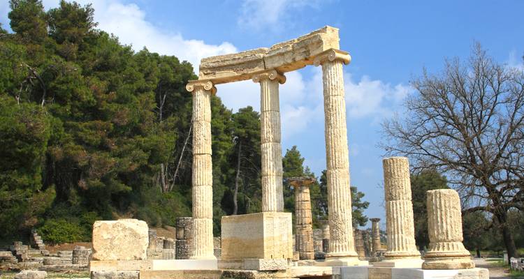 Ancient columns of a historic site with trees in the background.