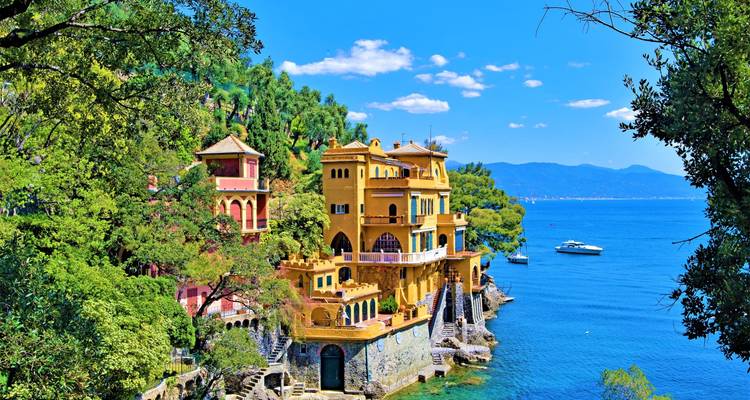 Villas colorées de Portofino perchées sur un promontoire boisé au-dessus de la mer Ligurienne bleue avec un yacht à proximité.