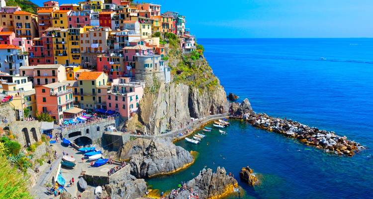 Maisons colorées au sommet des falaises de Manarola qui descendent en cascade vers un petit port dans les Cinque Terre avec une mer limpide.