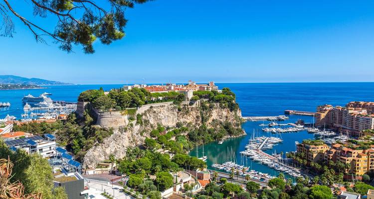 Panoramic view of Monaco’s cliff-top old town and mega-yacht harbour against deep blue Mediterranean.