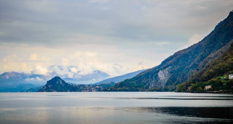 Moody view across Lake Maggiore towards misty mountains and lakeside villages beneath overcast skies.