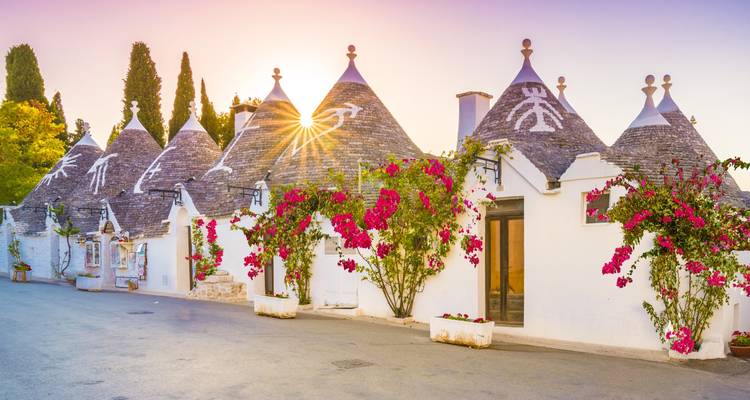 Rij van witgekalkte trulli huizen in Alberobello versierd met bougainvillea tijdens het gouden uur bij zonsondergang.
