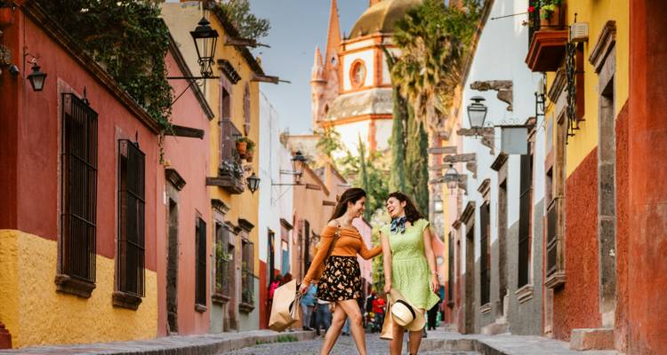 Deux femmes marchant dans une rue colorée avec une église en arrière-plan.
